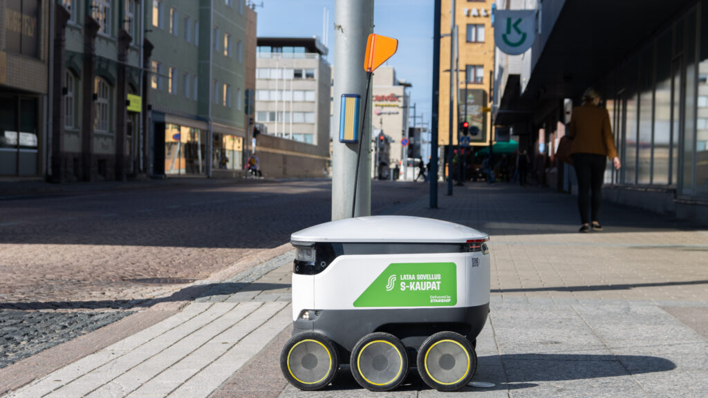 An Starship robot on the street with a green S-Kaupat sticker