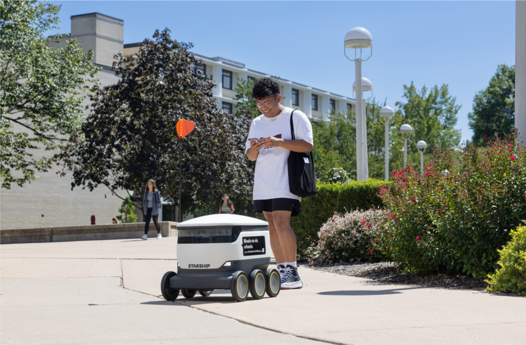 Student smiles while using Starship Delivery app to open the Starship robot lid and receive his order