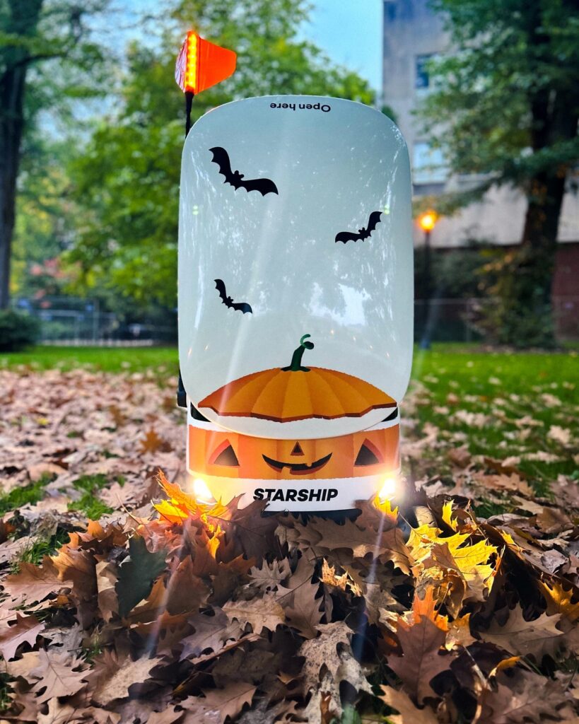 Starship robot wearing the seasonal stickers of a pumpkin as halloween costume