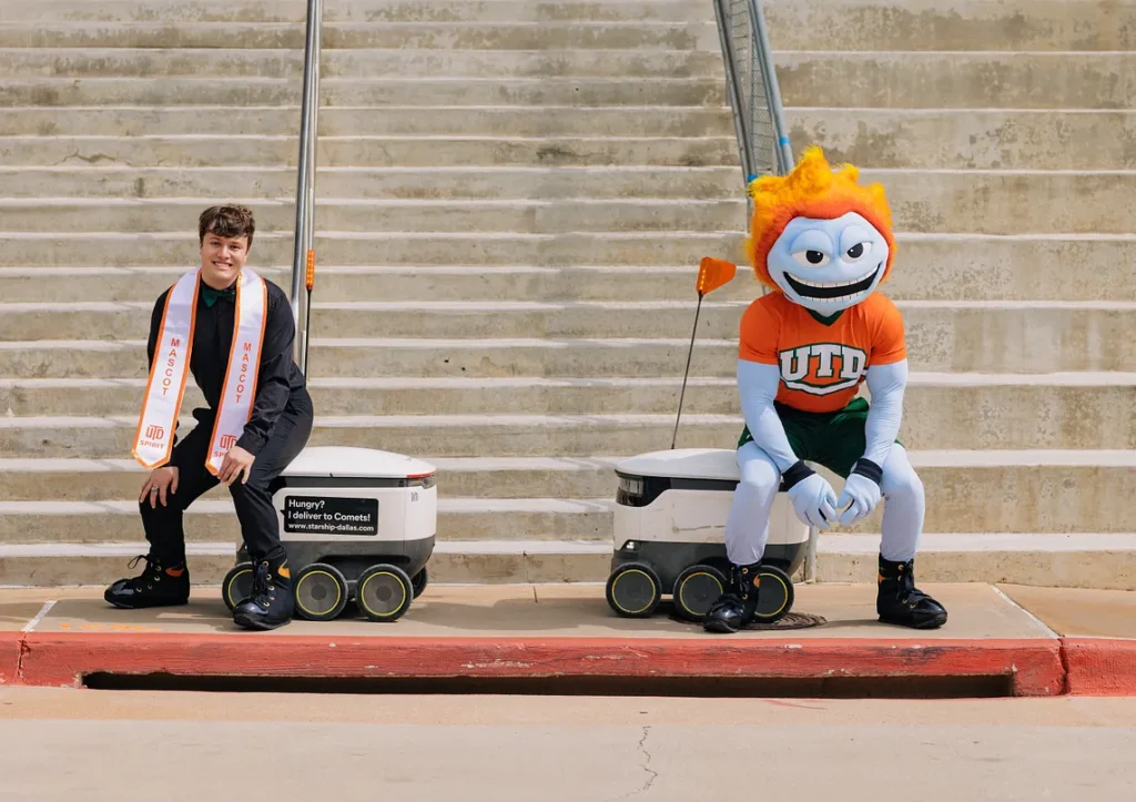 Graduate and UTD's mascot having fun with a Starship robot