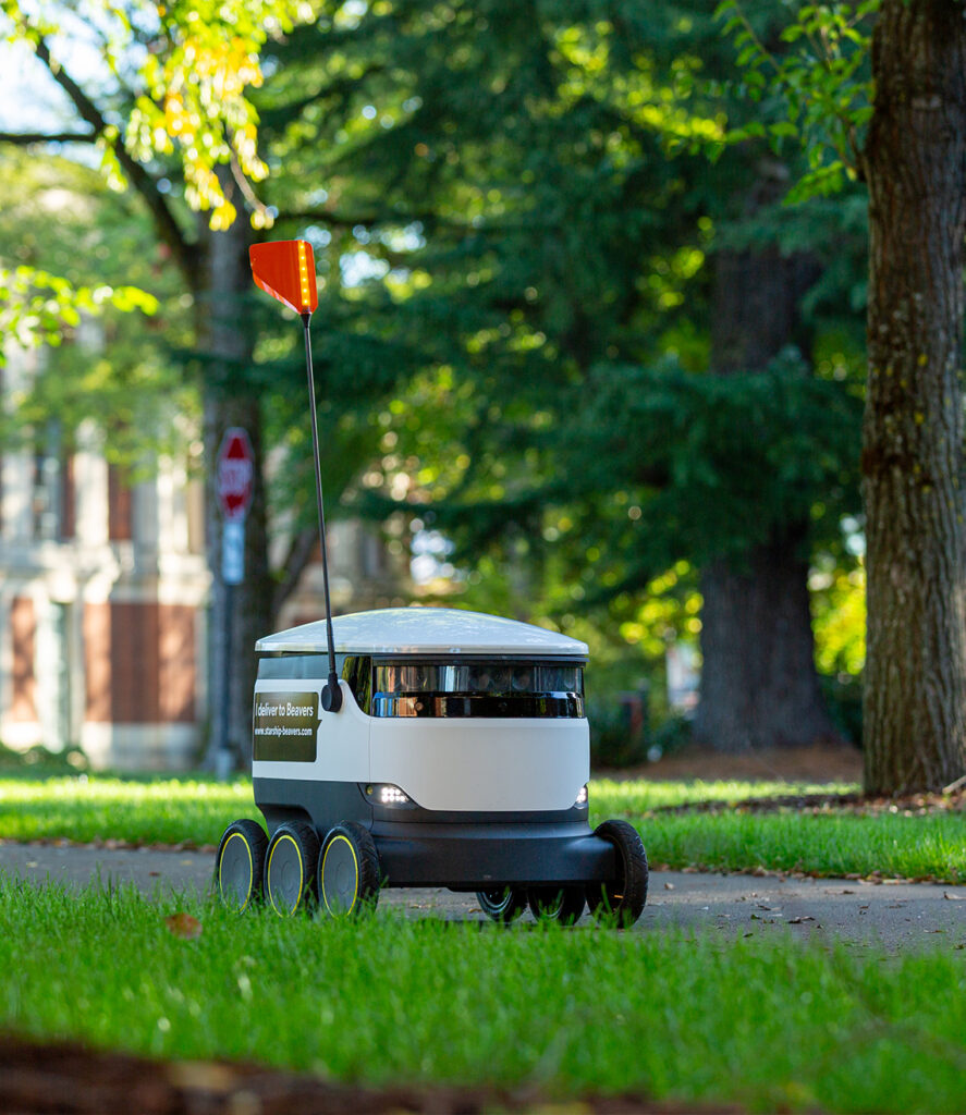 A Starship robot rolling through a park