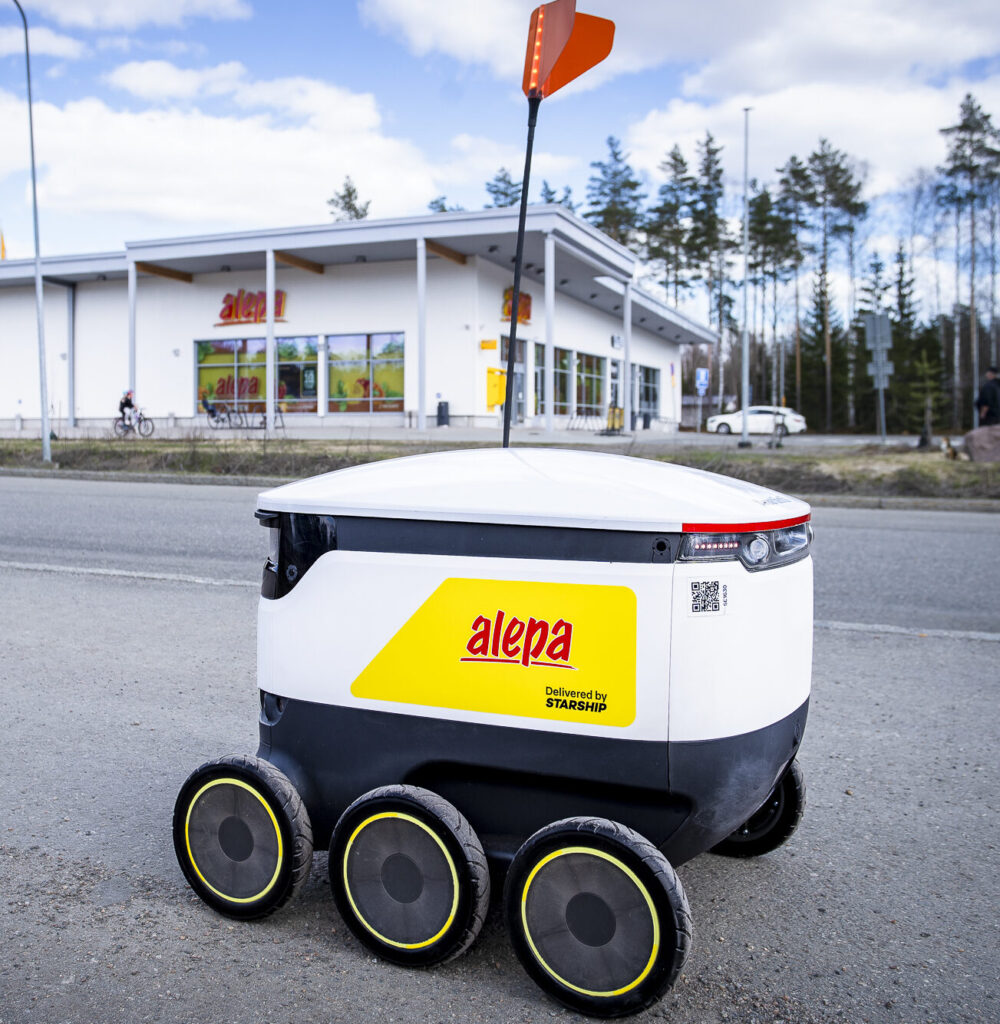 Starship robot with a yellow Alepa supermarket sticker rolling in the streets of Finland